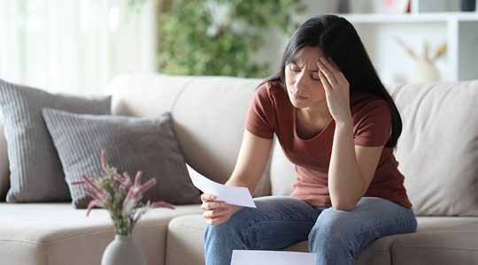 Worried woman checking letter on a sofa at home